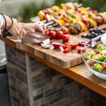 Garden table full of food ready for a barbeque party with a salad in the front and a woman cutting vegetable aside. garden table full of food ready for a barbeque party with a salad in the front and a woman cutting vegetable aside