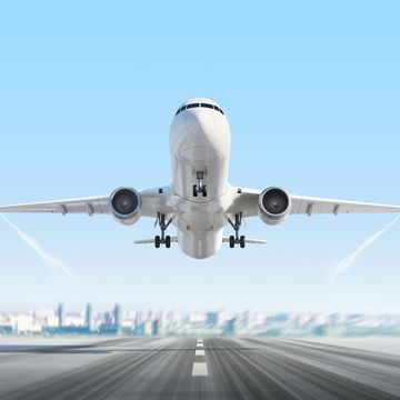 airplane taking off on a runway with jest streams in the blue sky and a skyline in the distance