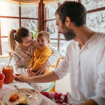 portrait of a cheerful young family having breakfast in their cottage house on the countryside, while it is snowing outside