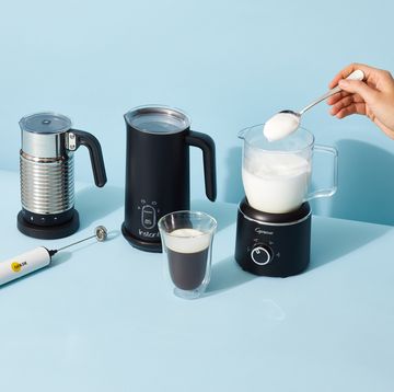 milk frothers from nespresso, instant, capresso and golde with a hand spooning some frothed milk onto a cup of coffee