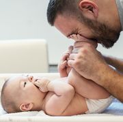 a dad cuddles his baby's feet after treating the baby with diaper rash cream and putting on a fresh diaper