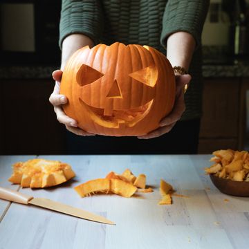 pumpkin carving, woman holding a carved smiley faced pumpkin over the table with a carving knife