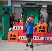 a minecraft themed trunk or treat setup features a big cardboard creeper, tnt and a kid dressed as steve