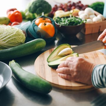 A woman cuts a ripe avocado and takes out a stone from it on a wooden plank. Fresh vegetables. Salad preparation. Diet food. Ecological products. a woman cuts a ripe avocado and takes out a stone from it on a wooden plank fresh vegetables salad preparation diet food ecological products