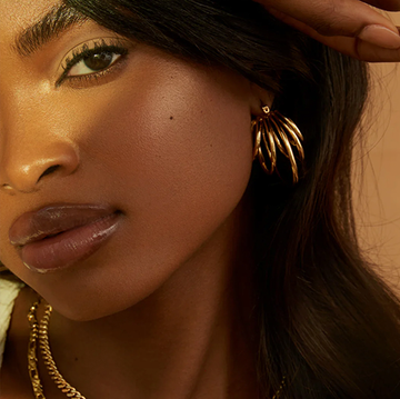 black owned jewelry brands, woman wearing gold earrings, woman wearing two gold bracelets