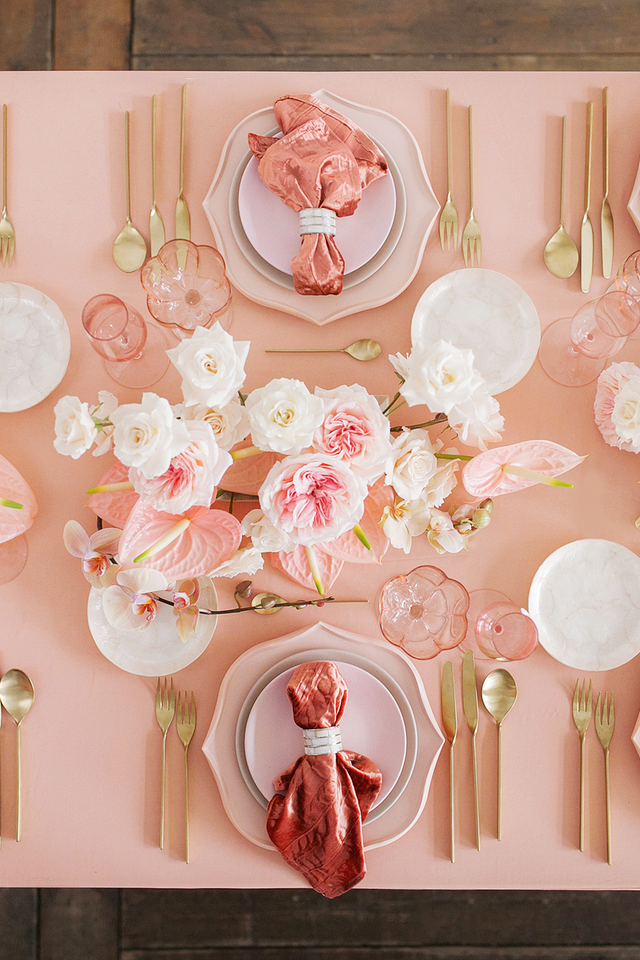 Valentine's Day Table Setting overhead view of pink and white flowers arranged on a pink tablecloth with pink and white dinnerware